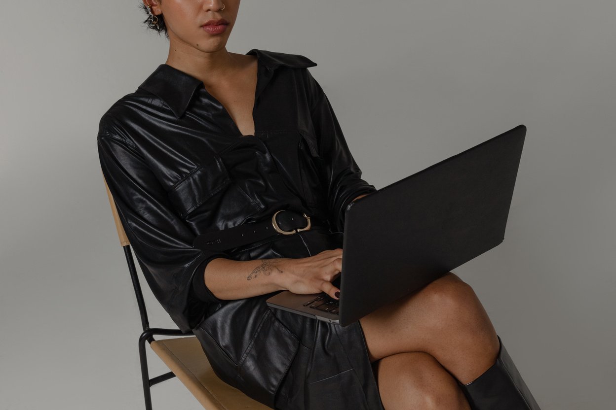 a person in a black leather dress sitting on a chair with a laptop